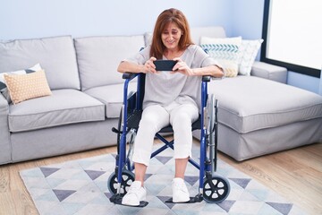 Wall Mural - Middle age woman watching video on smartphone sitting on wheelchair at home