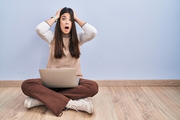 Sticker - Young brunette woman working using computer laptop sitting on the floor crazy and scared with hands on head, afraid and surprised of shock with open mouth