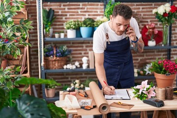 Poster - Young hispanic man florist talking on smartphone writing on document at florist