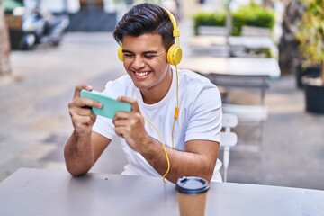 Sticker - Young hispanic man playing video game drinking coffee at coffee shop terrace