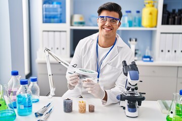 Sticker - Young hispanic man scientist looking sample with loupe at laboratory