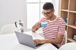 © Krakenimages.com - African american man using laptop drinking coffee at home