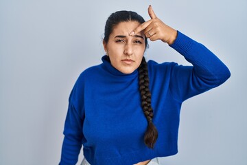 Poster - Young hispanic woman standing over isolated background pointing unhappy to pimple on forehead, ugly infection of blackhead. acne and skin problem