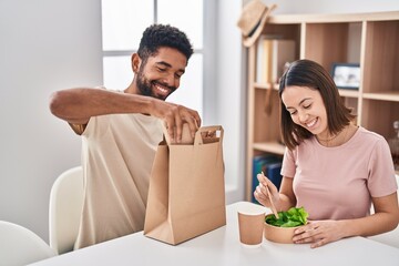 Poster - Man and woman couple sitting on table eating take away food at home