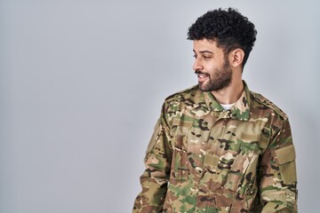 Sticker - Arab man wearing camouflage army uniform looking away to side with smile on face, natural expression. laughing confident.