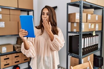 Canvas Print - Young hispanic woman working at small business ecommerce using tablet covering mouth with hand, shocked and afraid for mistake. surprised expression