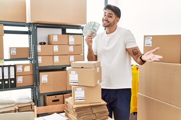Wall Mural - Young hispanic man working at small business ecommerce holding dollars celebrating achievement with happy smile and winner expression with raised hand