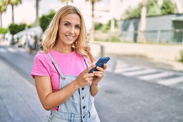 Wall Mural - Young blonde woman smiling confident talking on the smartphone at street