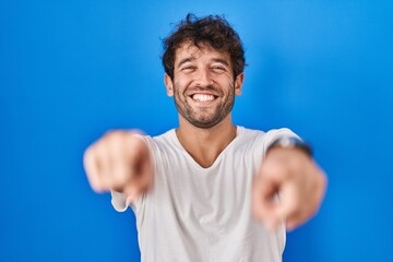 Canvas Print - Hispanic young man standing over blue background pointing to you and the camera with fingers, smiling positive and cheerful