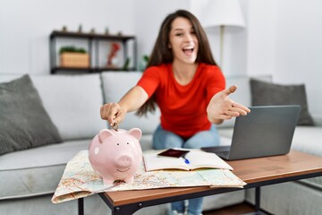 Wall Mural - Young brunette woman putting euro coin in piggy bank saving for travel celebrating achievement with happy smile and winner expression with raised hand