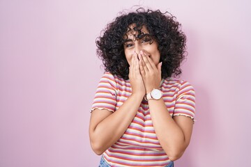 Sticker - Young middle east woman standing over pink background laughing and embarrassed giggle covering mouth with hands, gossip and scandal concept