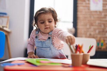 Poster - Adorable hispanic girl student sitting on table drawing on paper at kindergarten