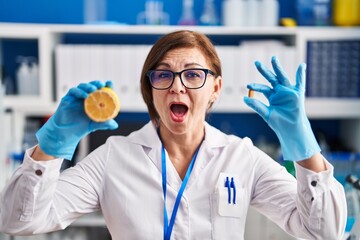 Sticker - Middle age hispanic woman working at scientist laboratory making vitamin afraid and shocked with surprise and amazed expression, fear and excited face.