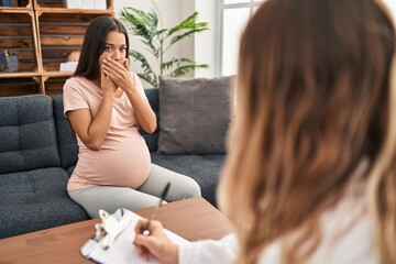 Canvas Print - Young pregnant woman at therapy session shocked covering mouth with hands for mistake. secret concept.