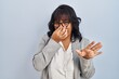 © Krakenimages.com - Hispanic woman standing over isolated background smelling something stinky and disgusting, intolerable smell, holding breath with fingers on nose. bad smell