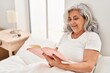 © Krakenimages.com - Middle age woman reading book sitting on bed at bedroom