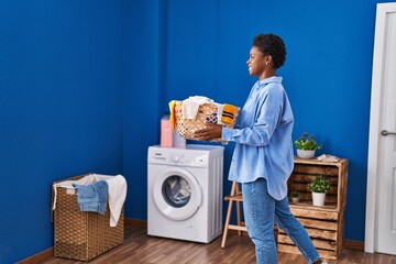 Wall Mural - African american woman smiling confident holding basket with clothes at laundry room
