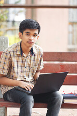 Wall Mural - Portrait of Indian boy using laptop while attending the online classes in park
