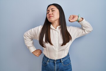 Sticker - Young latin woman standing over blue background stretching back, tired and relaxed, sleepy and yawning for early morning