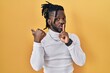 © Krakenimages.com - African man with dreadlocks wearing turtleneck sweater over yellow background asking to be quiet with finger on lips pointing with hand to the side. silence and secret concept.