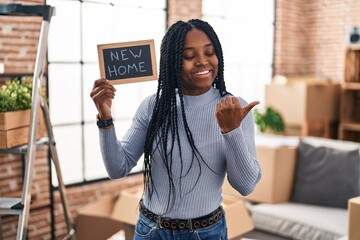 Canvas Print - African american woman holding blackboard with new home text pointing thumb up to the side smiling happy with open mouth