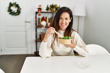 Sticker - Middle age hispanic woman eating salad sitting on the table by christmas decor at home