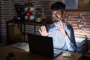 Poster - Young hispanic man with beard working at the office at night afraid and terrified with fear expression stop gesture with hands, shouting in shock. panic concept.