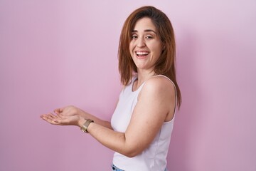 Sticker - Brunette woman standing over pink background pointing aside with hands open palms showing copy space, presenting advertisement smiling excited happy