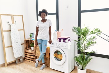 Sticker - African young woman doing laundry at home scared and amazed with open mouth for surprise, disbelief face