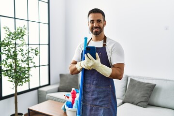 Wall Mural - Young hispanic man smiling confident wearing apron and cleaning gloves at home