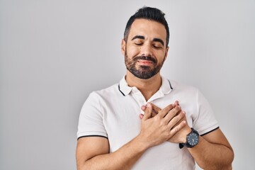 Canvas Print - Young hispanic man with beard wearing casual clothes over white background smiling with hands on chest with closed eyes and grateful gesture on face. health concept.