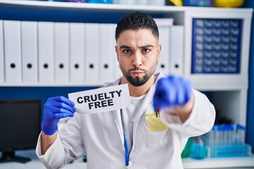 Poster - Young handsome man working at scientist laboratory holding cruelty free banner pointing with finger to the camera and to you, confident gesture looking serious