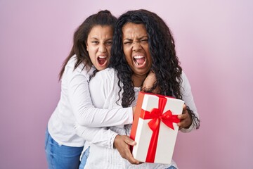 Sticker - Mother and young daughter holding with presents angry and mad screaming frustrated and furious, shouting with anger. rage and aggressive concept.