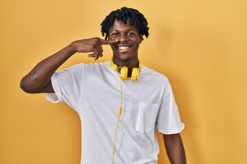 Canvas Print - Young african man with dreadlocks standing over yellow background pointing with hand finger to face and nose, smiling cheerful. beauty concept