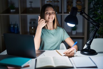 Canvas Print - Teenager girl doing homework at home late at night doing happy thumbs up gesture with hand. approving expression looking at the camera showing success.