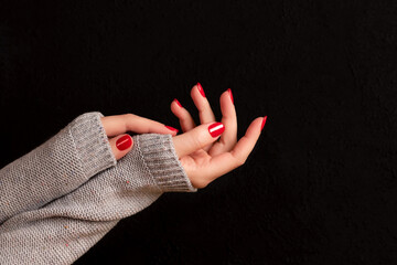 Wall Mural - Female hands in gray knitted sweater with beautiful manicure - red nails on dark black background. Nail care concept