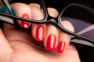 Wall Mural - Female hand with beautiful manicure - red nails with glasses on black background closeup