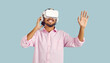 Virtual reality technology. Joyful young man enjoying using virtual reality glasses on pastel light blue background. Male VR user in pink shirt uses modern device for his entertainment. Web banner.