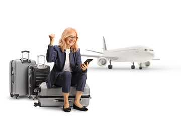 Poster - Woman sitting on a suitcase looking at a smartphone and gesturing happiness at an airport