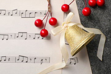 Wall Mural - Golden shiny bell with white bow, decorative berries and music sheets on grey textured table, flat lay and space for text. Christmas decoration