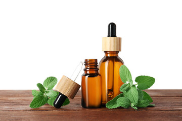 Bottles of essential oil and mint on wooden table against white background