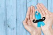 Prostate cancer concept. Hands with blue ribbon and mustache