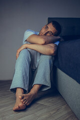 Dramatic lifestyle portrait of a handsome guy in his 30s and 40s, sitting sadly on the bed, feeling anxious and suffering from depression. Attractive depressed and upset man in home bedroom.