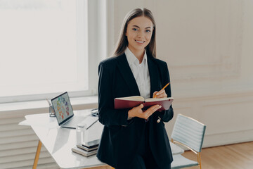 Wall Mural - Female director holding notebook and pencil while leaning on office desk