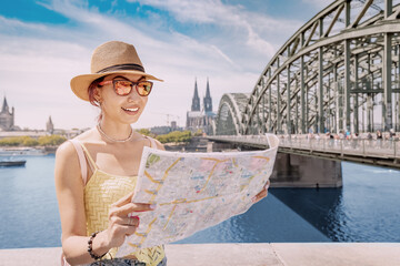 tourist girl with map, searching for landmarks and sights in old European city with bridge over Rhine river and Cologne cathedral in the background