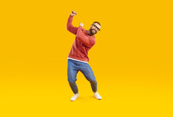 Wall Mural - cheerful, joyful and carefree man is having fun dancing on orange background in studio. handsome and