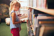 Schoolgirl Looking For Book For Reading In School Library. Student Choosing Literature For Reading. Books On Shelves In Bookstore. Learning From Books. Back To School. Elementary Education