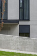 Detal na obiekt biurowy. Elewacja wykonana z tynku i akcentami betonu. Harmonijny i spójny układ okien. Spadek terenu z zejściem.