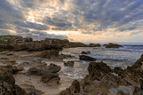 Fototapeta Morze - rocky cove and sandy beach under an expressive sunset sky on the rugged west coast of Sardinia