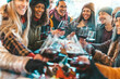 © Davide Angelini - Happy multiracial friends toasting red wine at restaurant balcony - Group of young people wearing winter clothes having fun at winebar table - Dining life style and friendship concept